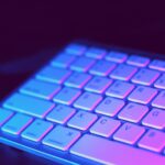 Close-up of a modern keyboard illuminated with vibrant purple and blue neon lighting.